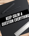 Black mat with 'Keep Calm & Question Everything' text, pen, and ruler on a wooden surface