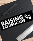 Sticker with 'RAISING REPUBLICANS' text and footprints on a black background, placed on a wooden surface with pens and a ruler.
