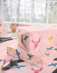 Gift wrapped in blush pink paper with watercolor birds in flight and floating feathers.