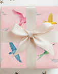 Bird wrapping paper design with green, pink, and yellow birds against a soft pink background.