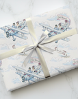 Wedding gift wrap featuring a bride and groom in a small airplane with just married banner and soft clouds, on a marble surface with a silver bow.