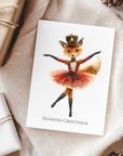 Greeting card with a fox character in a ballet outfit on a textured surface with gift wraps and pine cones.