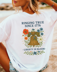 Woman wearing a white t-shirt with a graphic design of a liberty bell and flowers including text that says ringing true since 1776