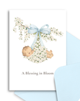 Greeting card with baby-themed design featuring a baby hanging from an apple tree branch, tied with a blue ribbon, on a white background.