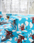 Wrapping paper with a pattern of red biplanes flying through a blue sky with white clouds.