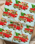 Christmas gift wrap on a light aqua background featuing santa driving a classic 1957 Chevy.