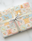 Storybook style baby wrapping paper with quilt pattern featuring teddy bears moons and nursery icons.