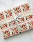 Gift wrapped in Valentine's Day-themed paper with cherub stamp illustrations on a white marble surface.