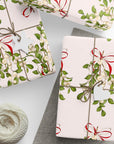 Vintage mistletoe wrapping paper with green leaves and red bows on blush background