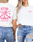 Woman wearing a white t-shirt with hot pink text that says 1776 vibes trust in God with muskets and an American flag on the back and on the front is a graphic that says 1776 back and front view
