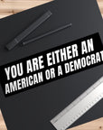 Black bumper sticker with text 'YOU ARE EITHER AN AMERICAN OR A DEMOCRAT' on a black surface with pens and a ruler.