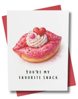 Funny romantic Valentine’s Day card featuring a pink donut shaped like lips with whipped cream and candy hearts and the phrase You're My Favorite Snack.