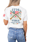 woman wearing a white t-shirt with patriotic design crossed muskets floral adorned with a betsy ross flag trust in god text back design