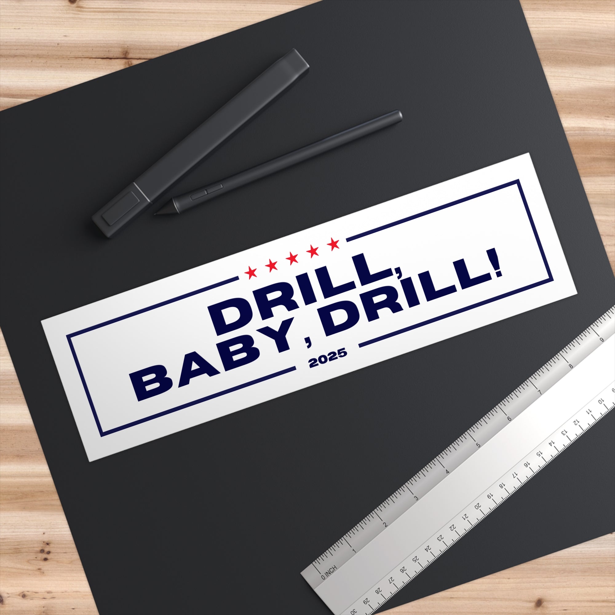 Sticker with 'DRILL BABY, DRILL! 2025' text on a black surface with pens and a ruler.