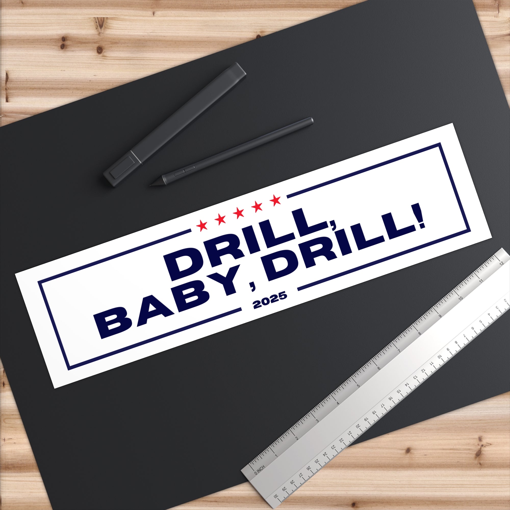Sticker with 'DRILL, BABY, DRILL! 2025' text on a black surface with a ruler and pens.