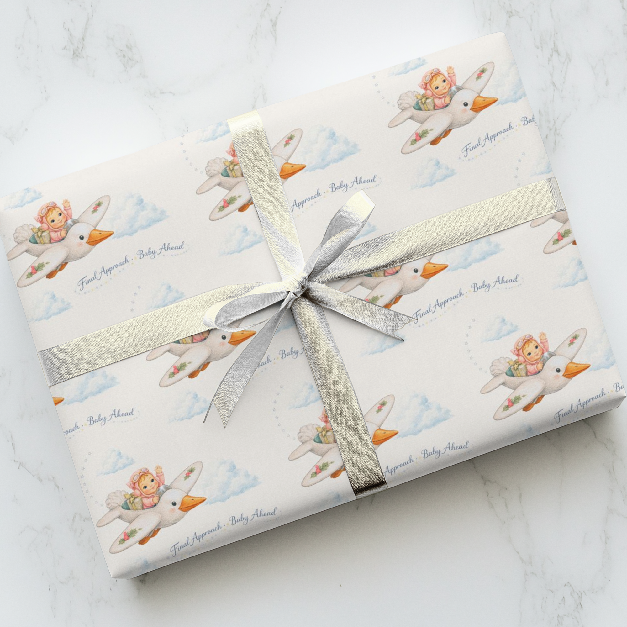 Gift wrapped in baby-themed paper with a silver ribbon on a marble surface