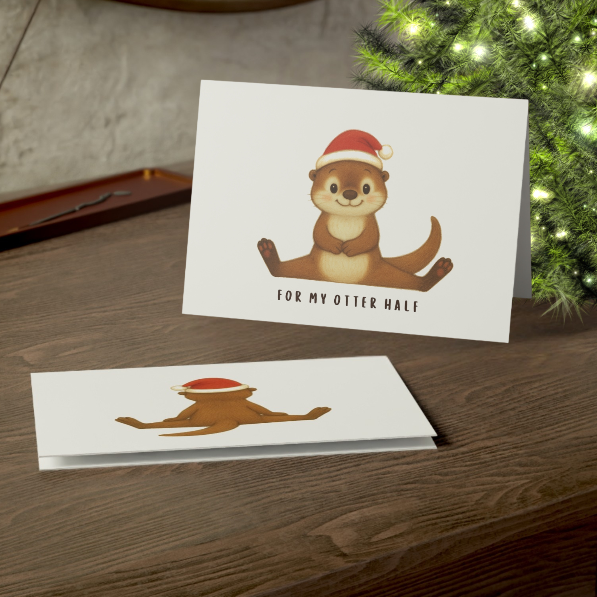 Christmas card with an otter wearing a Santa hat on a wooden surface with a Christmas tree in the background.