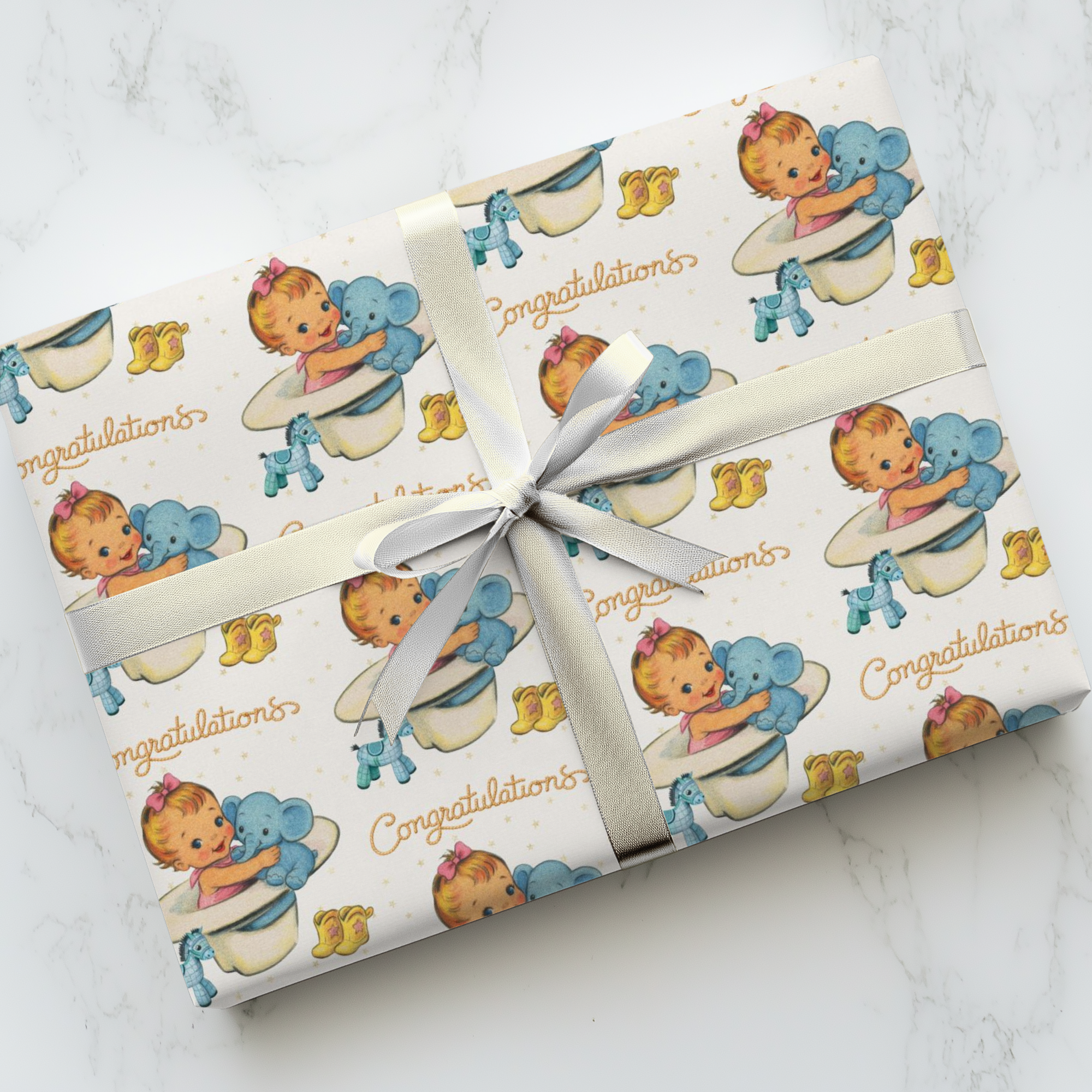 Gift wrapped in cowgirl baby-themed paper with a white ribbon on a marble surface
