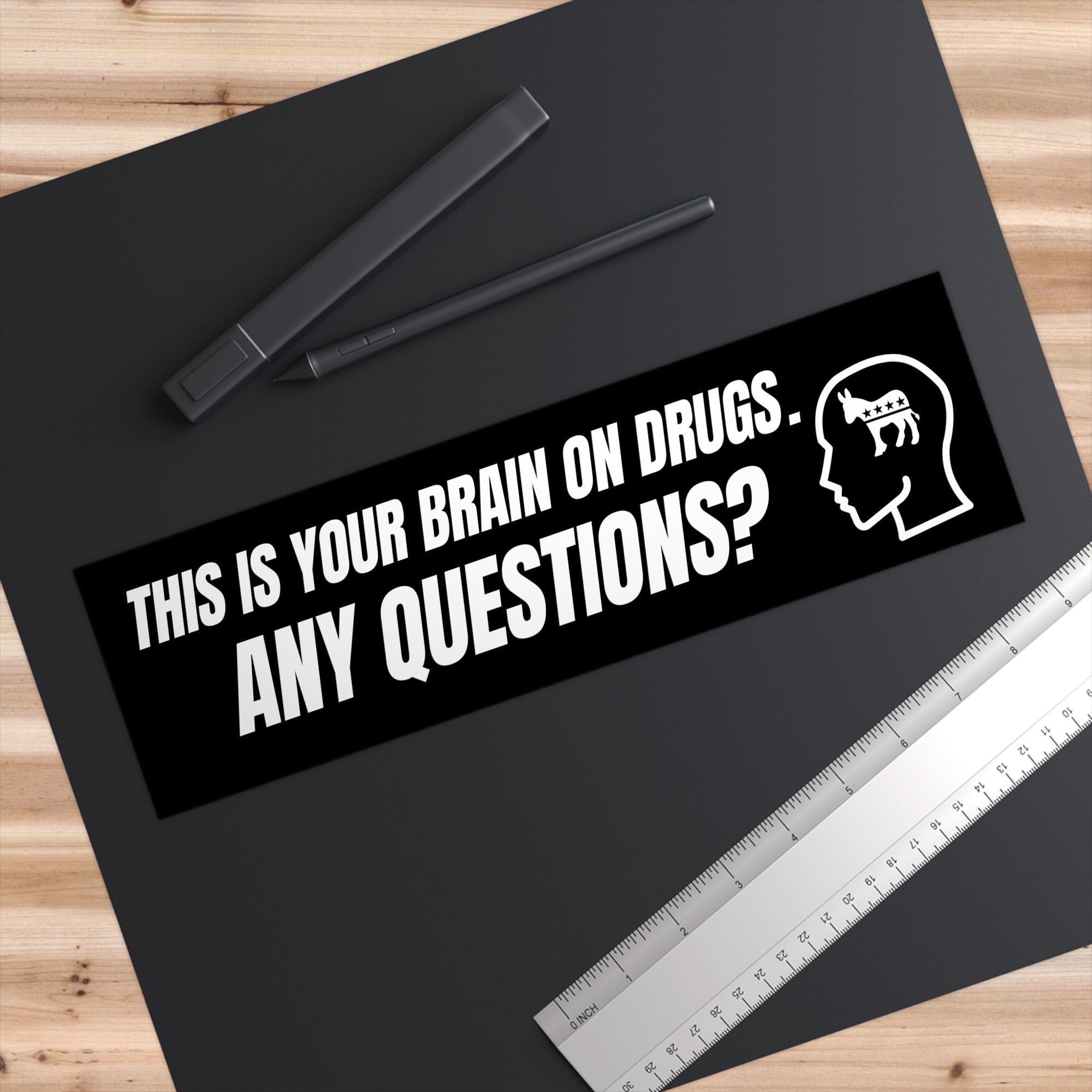 Sticker with text 'This is your brain on drugs. Any questions?' on a black background with pens and a ruler.