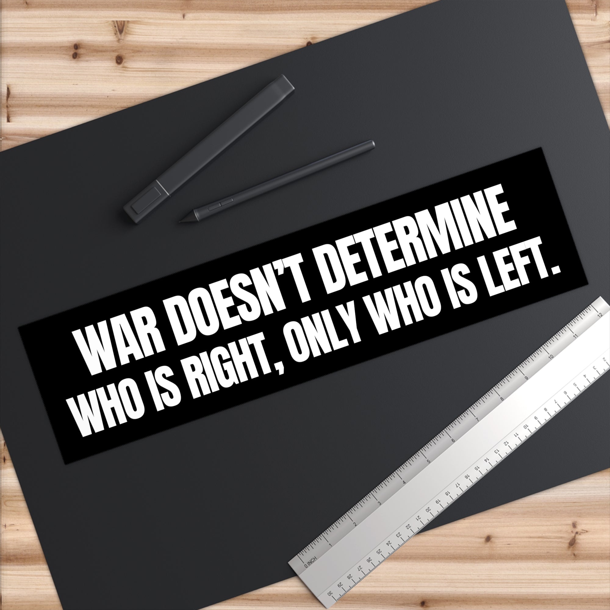 Black bumper sticker with white text on a black surface with a pen and ruler.