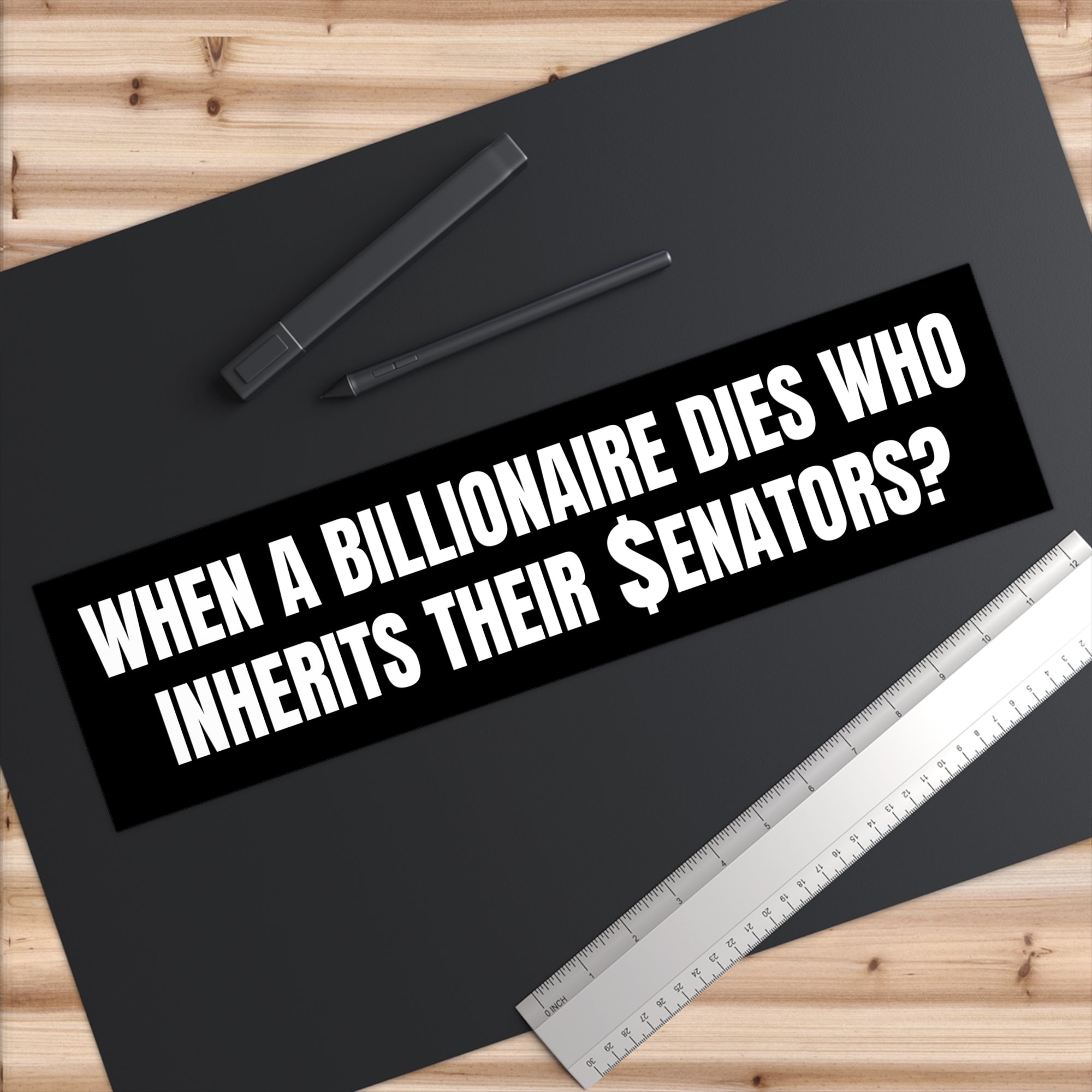 Black bumper sticker with humorous text on a black surface with a pen and ruler.