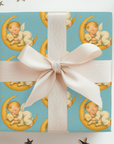 Gift box wrapped with new baby sleeping on a crescent moon design with a white ribbon on a white background.