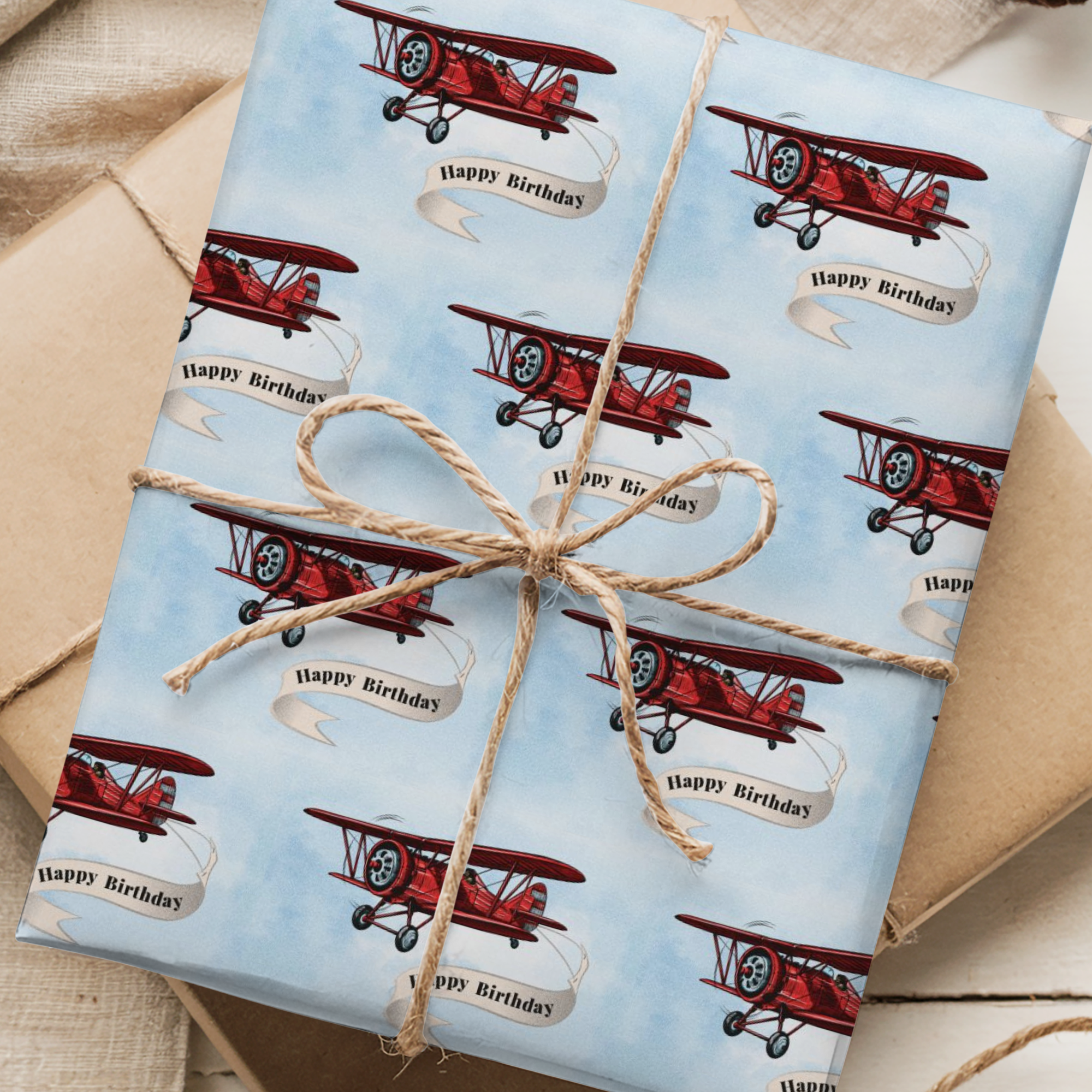 Wrapping paper featuring a classic red vintage biplane towing a cream-colored banner that reads “Happy Birthday”