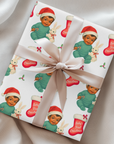 Vintage “Baby’s First Christmas” wrapping paper featuring a smiling dark-skinned baby in a mint green romper and Santa hat holding a white bunny plush and candy cane, surrounded by red Christmas stockings and holly, retro storybook illustration style.