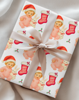 Vintage “Baby’s First Christmas” wrapping paper featuring a smiling blonde baby girl in a pink romper and Santa hat holding a white bunny plush and candy cane, surrounded by red Christmas stockings and holly, retro storybook illustration style.