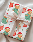 Vintage-style Baby’s First Christmas wrapping paper featuring a smiling blonde baby in a mint green romper and Santa hat holding a white bunny plush and candy cane, surrounded by red Christmas stockings and holly, retro storybook style.