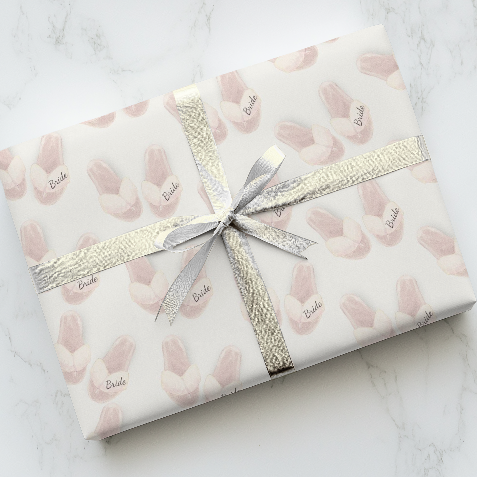 Gift wrapped in 'Bride' patterned paper with a silver ribbon on a marble surface.