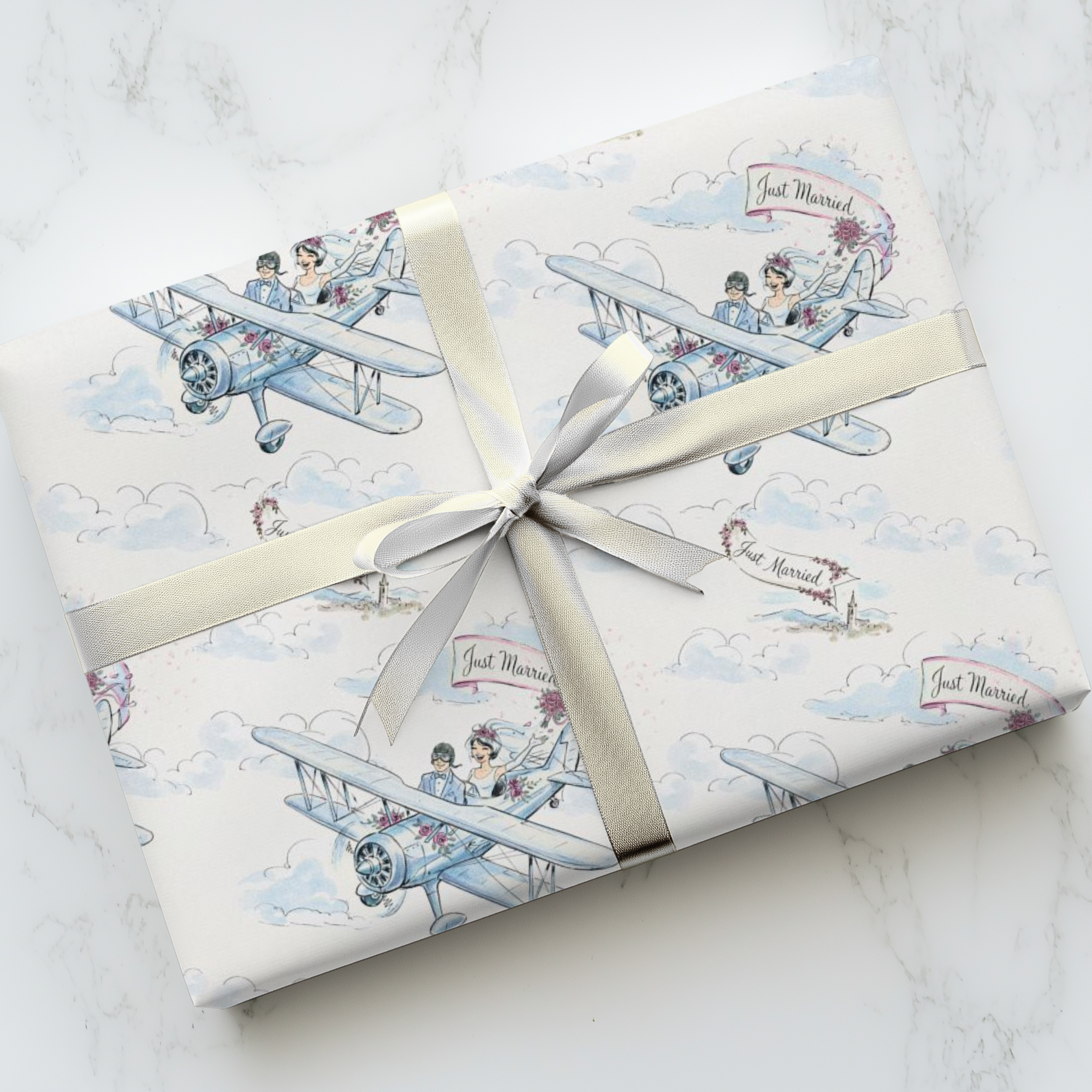 Wedding gift wrap featuring a bride and groom in a small airplane with just married banner and soft clouds, on a marble surface with a silver bow.