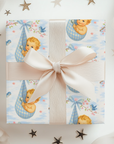 Gift box with baby-themed wrapping paper and a pink ribbon, surrounded by decorative stars.