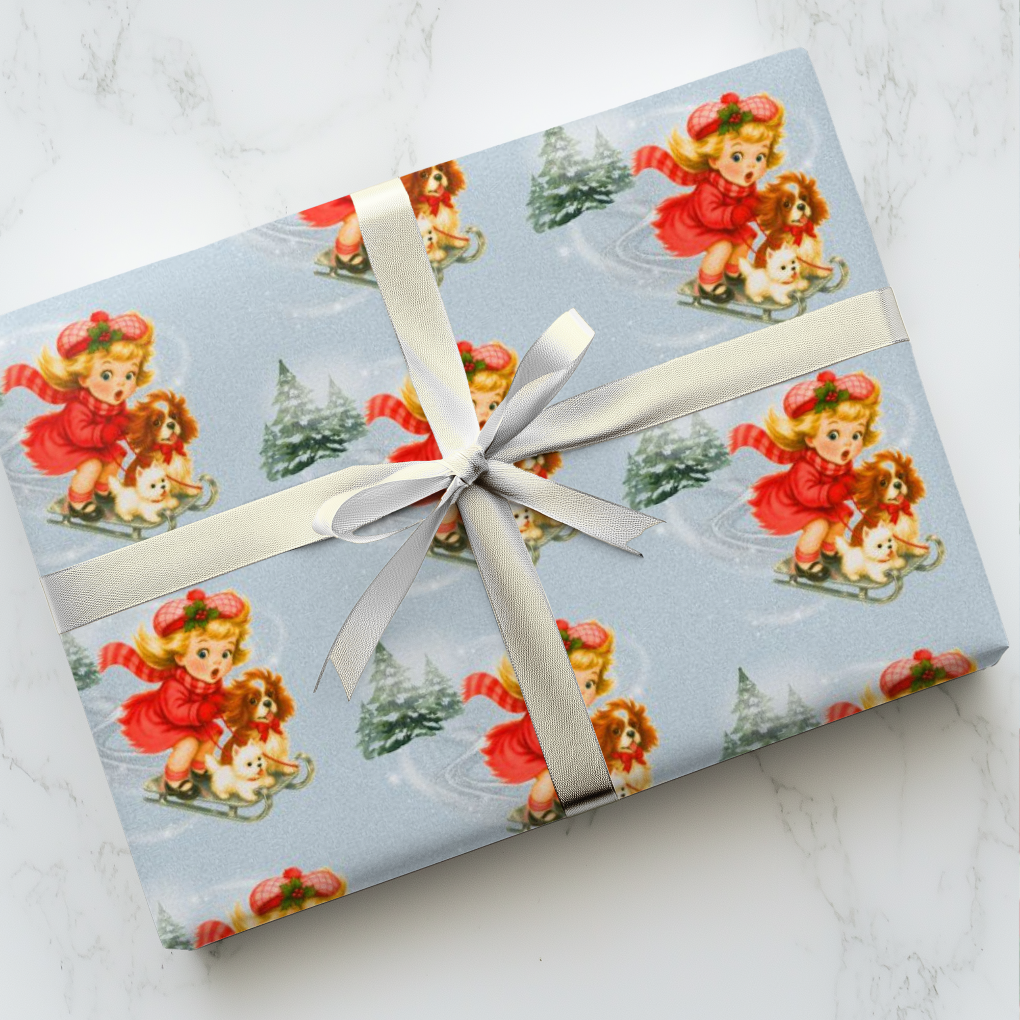Vintage Christmas wrapping paper little girl sledding with westie and cavalier dogs on pale blue background with snowy pine trees.