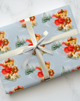 Vintage Christmas wrapping paper little girl sledding with westie and cavalier dogs on pale blue background with snowy pine trees.