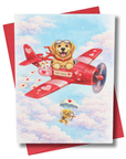 Greeting card with a golden retriever in a red airplane and a puppy with a parachute, set against a blue sky with clouds.