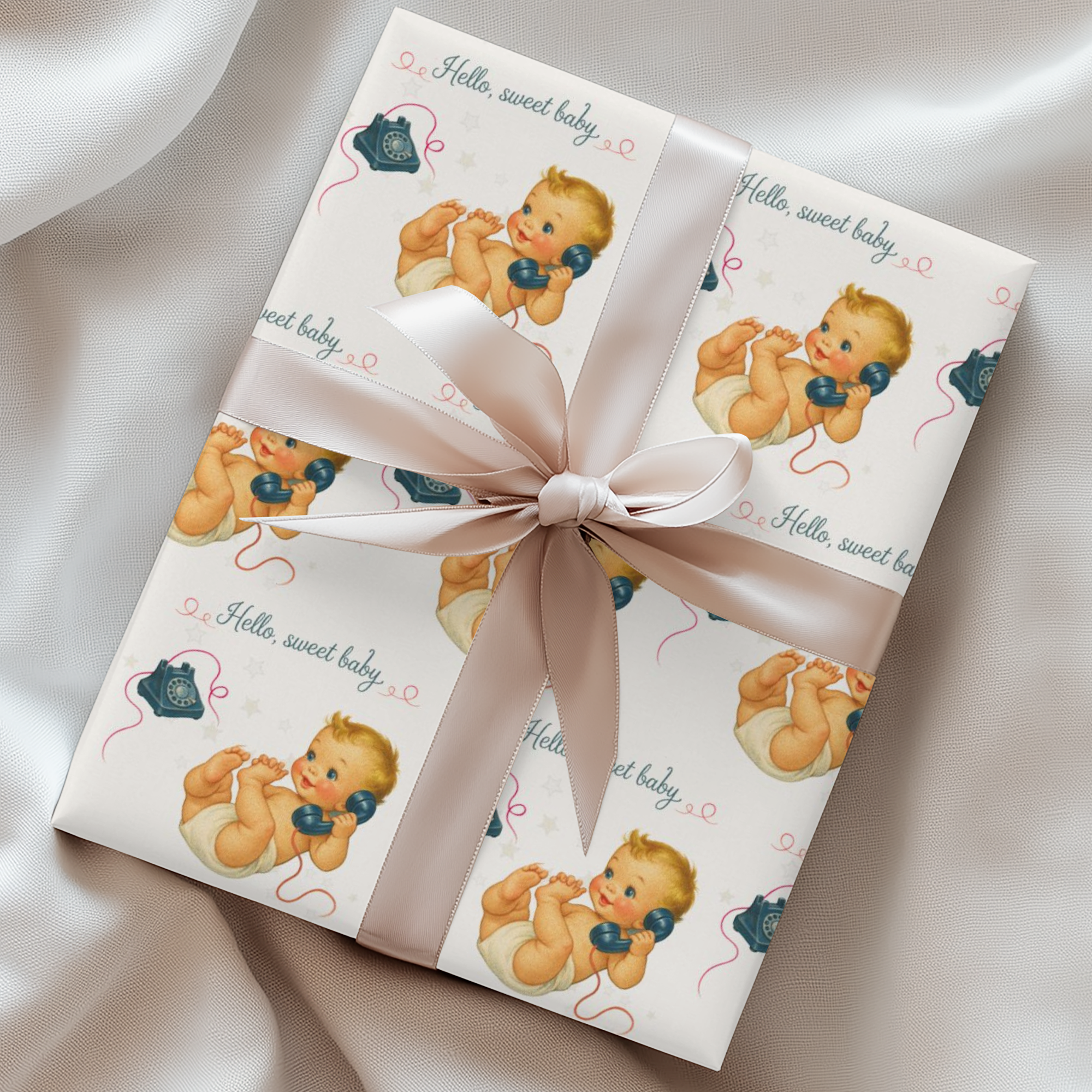 Gift wrapped in baby-themed paper with a bow on a satin surface
