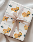 Gift wrapped in baby-themed paper with a bow on a satin surface
