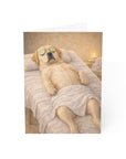 greeting card featuring a labrador retriever dog with cucumbers on eyes and a towel draped over it, lying on a massage table.
