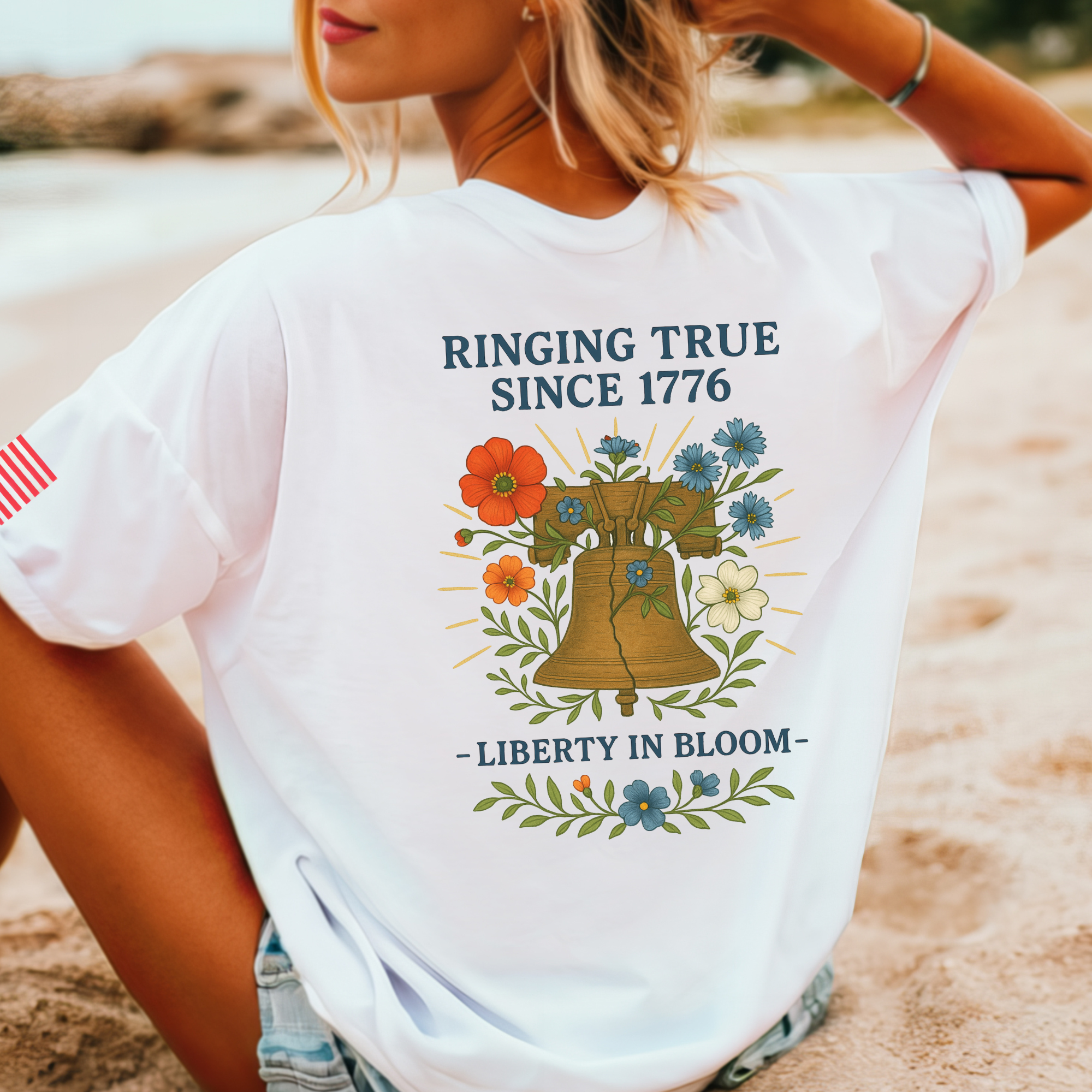 Woman wearing a white t-shirt with a graphic design of a liberty bell and flowers including text that says ringing true since 1776