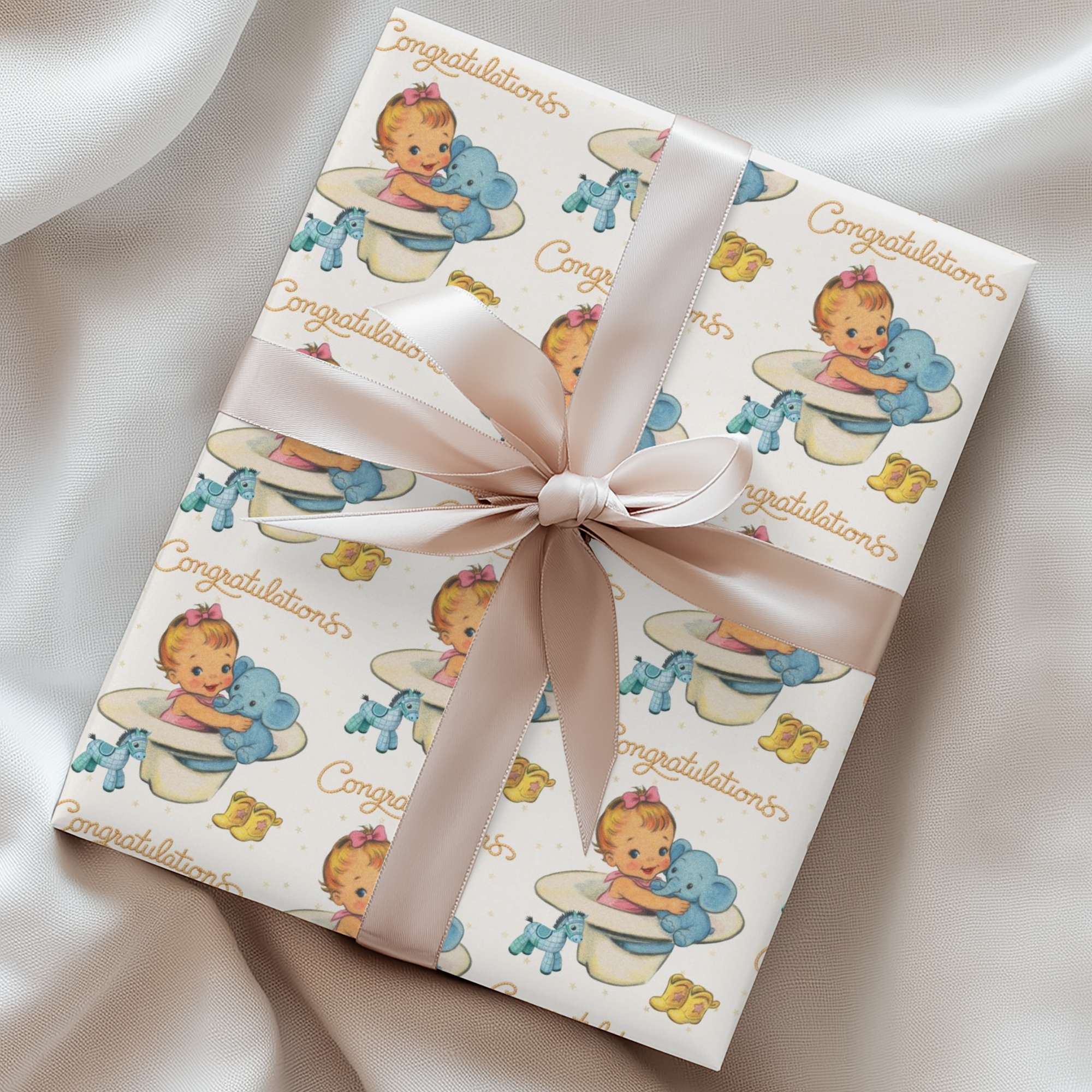 Gift wrapped in western baby-themed paper with a pink ribbon on a satin surface