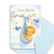 New baby card with a baby in a blue checkered sling, birds, and cherry blossoms on a light blue background.