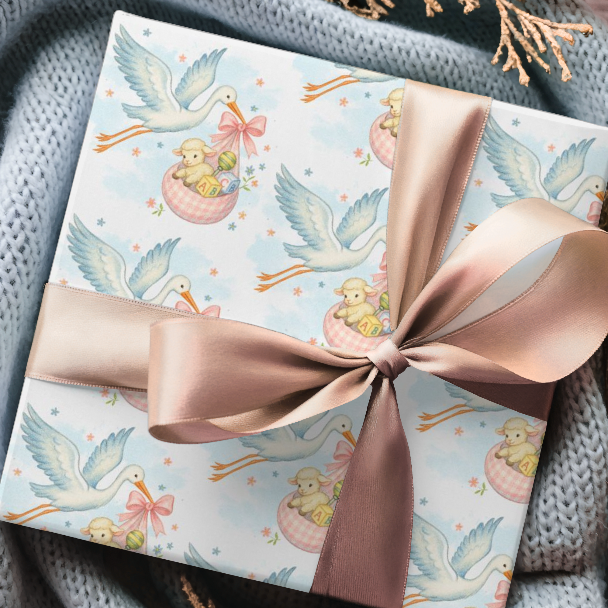 Gift wrapped in paper with stork and baby design, tied with a pink ribbon on a textured surface.