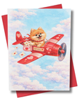 Greeting card featuring a Pomeranian dog in a red airplane against a blue sky with clouds