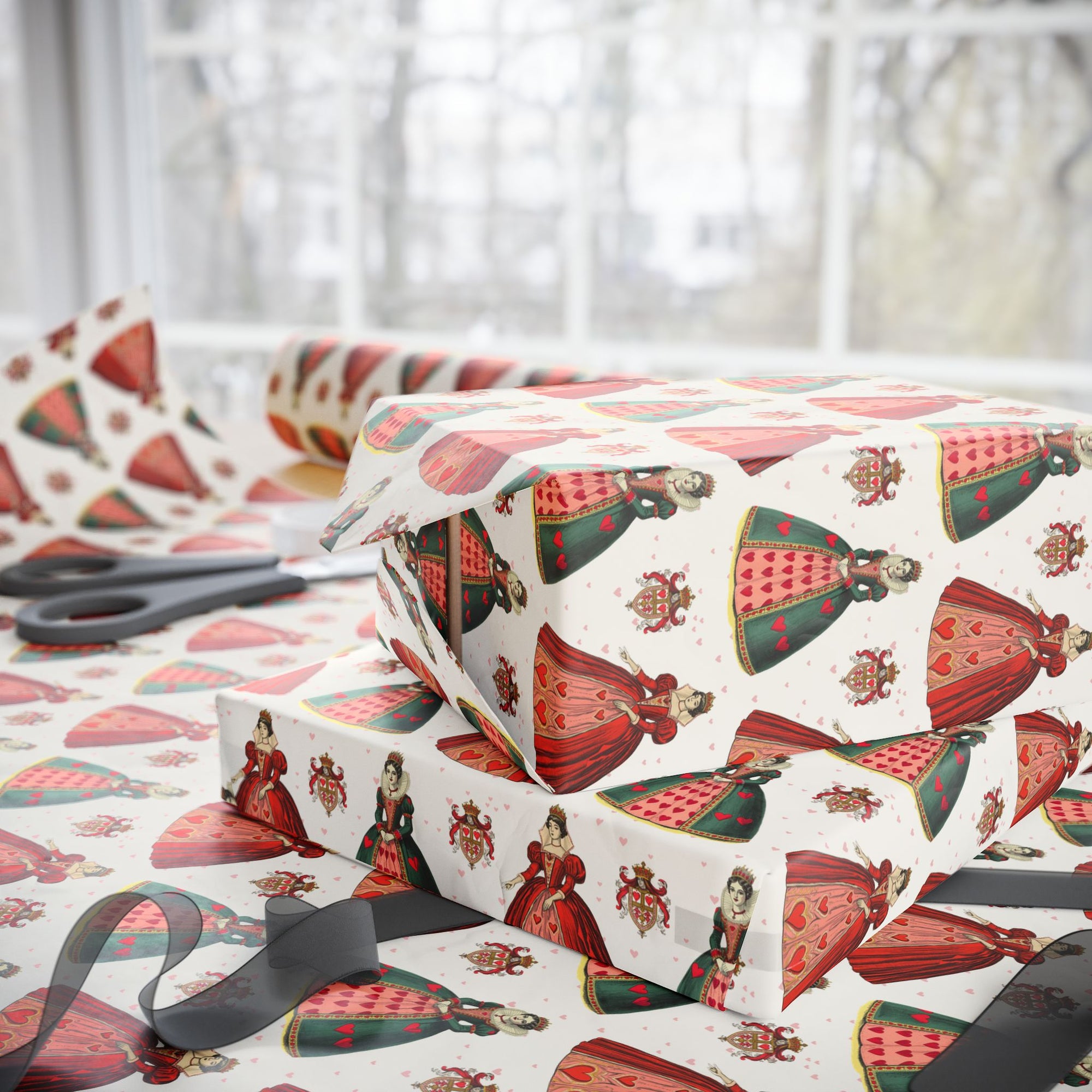 Gift boxes wrapped in queen of hearts themed paper with scissors on a table.