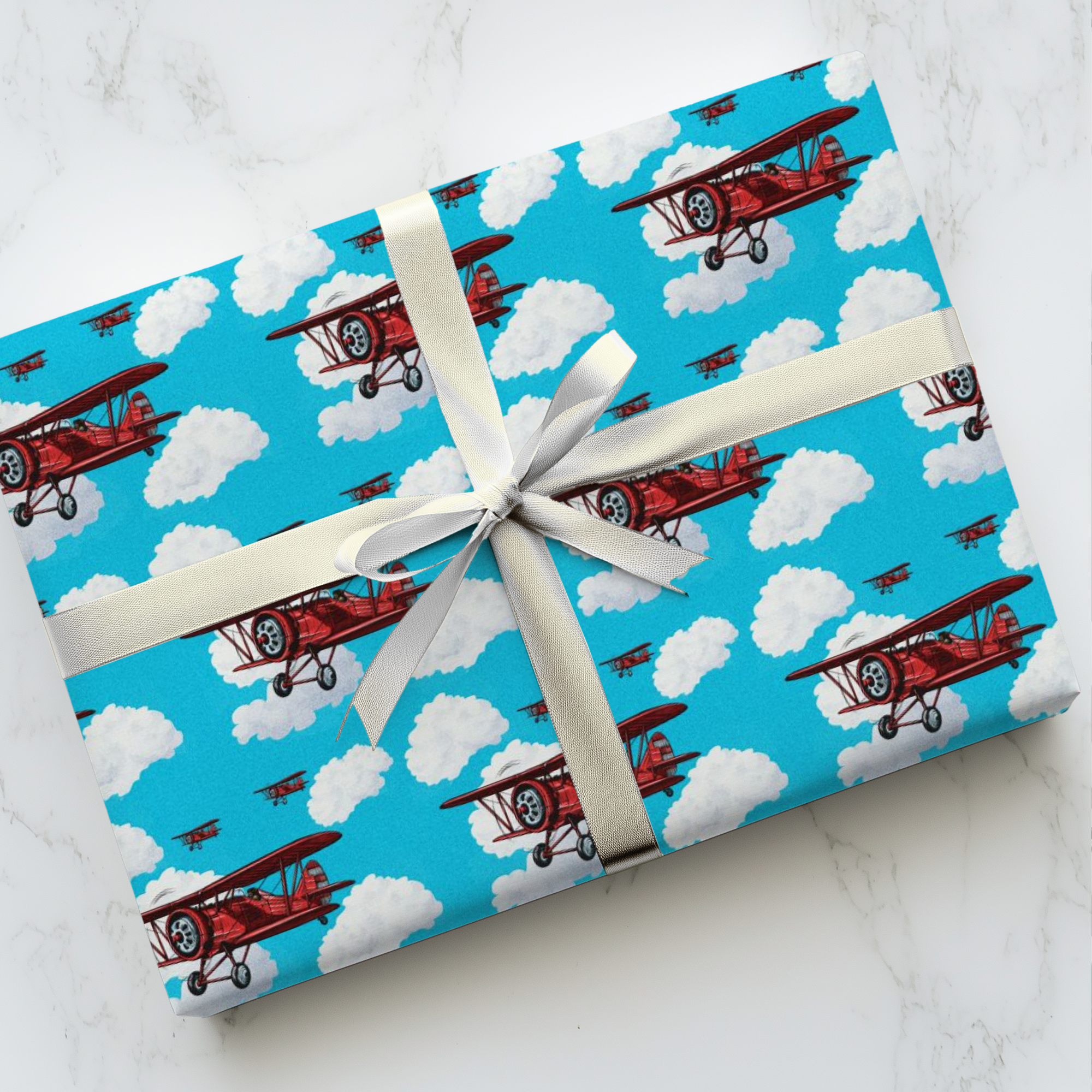 Wrapping paper with a pattern of red biplanes flying through a blue sky with white clouds.