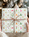 Gift wrapped in festive paper with Christmas-themed illustrations held by hands against a blurred Christmas tree background.