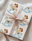 Gift wrapped in paper with a child's illustration of a baby on a rocking horse, tied with a ribbon.