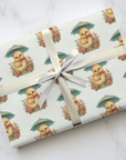 Gift wrapped in paper featuring a baby chick holding a parasol in the rain on a light background.