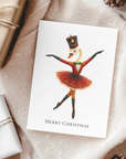 Christmas card with a swan dancer design on a textured surface with gift wraps and pine cones.